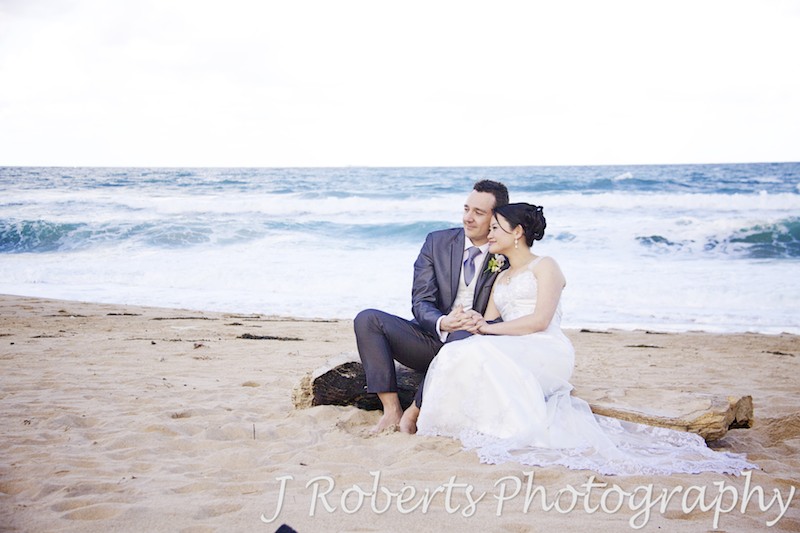 Couple sitting on driftwood at the beach - wedding photography sydney